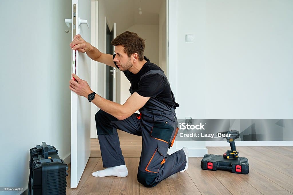Man installing interior door using spirit level. Professional craftsman in uniform aligning door with tools during home renovation