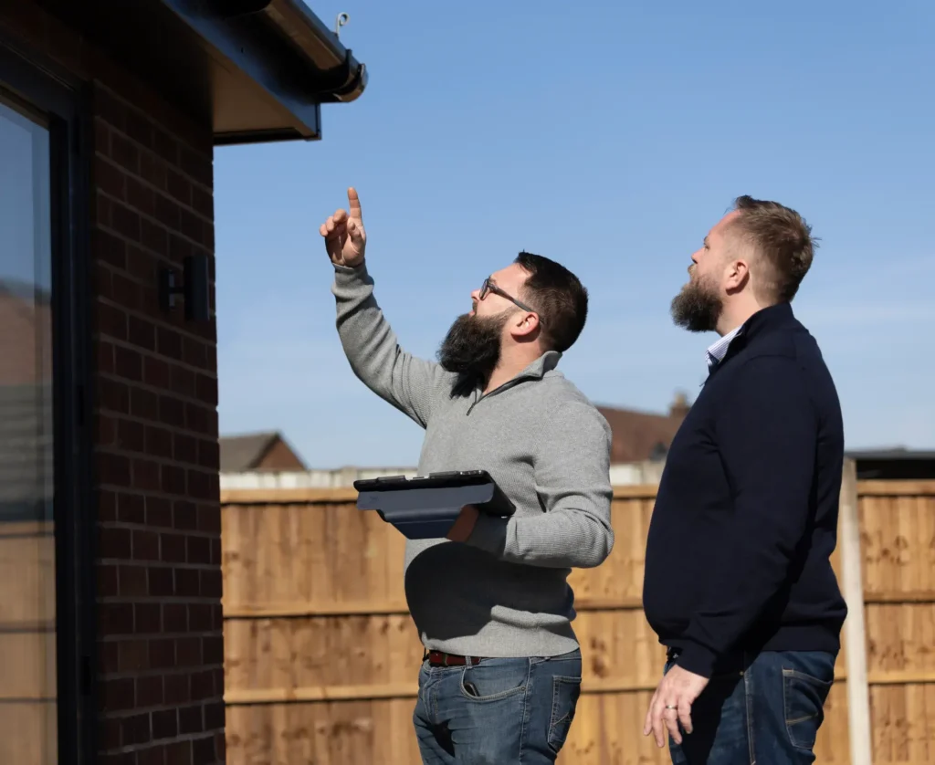Men evaluating the exterior of a building under clear blue skies.